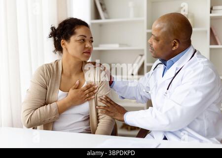 Medico compassionevole che mette mano sulla spalla dei pazienti femminili durante la consultazione medica Foto Stock