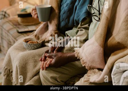 Coppia multietnica anziana seduta insieme tenendosi per mano e bevendo un caffè Foto Stock
