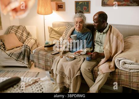 Donna caucasica anziana e uomo Nero anziano seduti insieme a bere tè Foto Stock