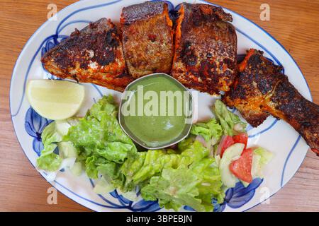 Pesce di trota Tandoori alla griglia alla perfezione, servito con chutney verde piccante, spicchi di limone e insalata verde fresca. Un saporito piatto indiano Foto Stock
