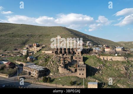 Vista aerea di edifici in pietra e case residenziali su una collina nel villaggio di Arzakan, provincia di Kotayk, Armenia. Il paesaggio comprende pendii verdi Foto Stock
