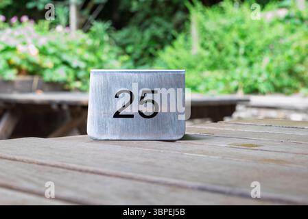 Un tavolo di metallo numero 25 si trova su un tavolo in legno per esterni, utilizzato per identificare la posizione specifica dei posti a sedere per i clienti o il personale di assistenza. Foto Stock