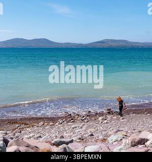 Waterville Beach, Count Kerry, Repubblica d'Irlanda: Affacciata sulla baia di Ballinskelligs. Una bella giornata di sole. Una donna solitaria passeggia fino al bordo delle acque Foto Stock