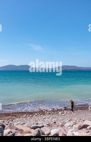 Waterville Beach, Count Kerry, Repubblica d'Irlanda: Affacciata sulla baia di Ballinskelligs. Una bella giornata di sole. Una donna solitaria passeggia fino al bordo delle acque Foto Stock