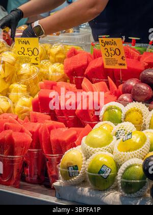 Coppette di frutta fresca tagliate, tra cui anguria (sandía) e ananas (piña), in vendita presso un colorato chiosco del mercato la Boqueria, Barcellona, Spagna. Foto Stock