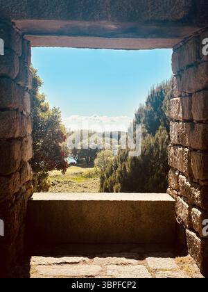 Antica arcata in pietra che incornicia un paesaggio rurale illuminato dal sole di colline e alberi nella regione di Porto, Portogallo, rovine storiche e campagna panoramica Foto Stock