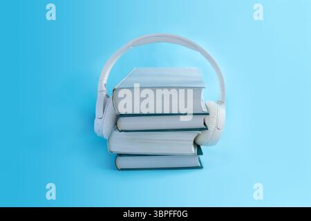 Cuffie wireless bianche su una pila di libri su sfondo azzurro. Concetto per audiolibri in stile minimalista. Foto Stock