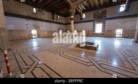 Una camera spaziosa e vuota con pavimenti geometrici intricati, soffitto in legno e finestre ad arco. La camera dispone di una fontana centrale. Antico Alep Foto Stock