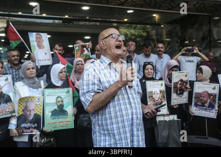 Nablus, Palestina. 8 luglio 2025. Un uomo canta slogan attraverso un microfono mentre famiglie di prigionieri palestinesi tengono le foto dei loro parenti imprigionati durante una manifestazione di solidarietà. I palestinesi hanno organizzato una protesta per chiedere un accordo di scambio di prigionieri con il governo israeliano e Hamas. Credito: SOPA Images Limited/Alamy Live News Foto Stock