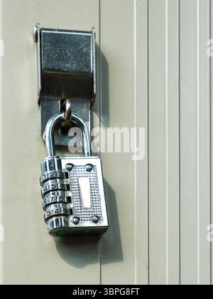 Un lucchetto a combinazione in metallo lucido è fissato saldamente su un pannello della porta beige, a simboleggiare la sicurezza e l'accesso limitato Foto Stock
