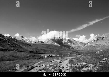Vista alpina con una strada rocciosa che conduce al piccolo lago di montagna e alle cime innevate. Parco nazionale della Vanoise. (Savoia, Francia) Foto Stock