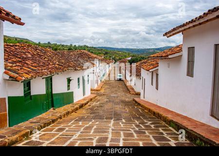 Una vista pittoresca di una strada lastricata di pietra fiancheggiata da tradizionali case bianche a Barichara, Santander, che mostra il fascino coloniale della città. Foto Stock