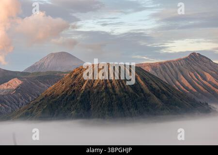 Vista dei maestosi vulcani illuminati dal sole che piergono attraverso un mare di nuvole eteree, creando uno stupefacente contrasto tra terra e cielo, vulcano del Monte Bromo, Giava Orientale, Indonesia. Foto Stock