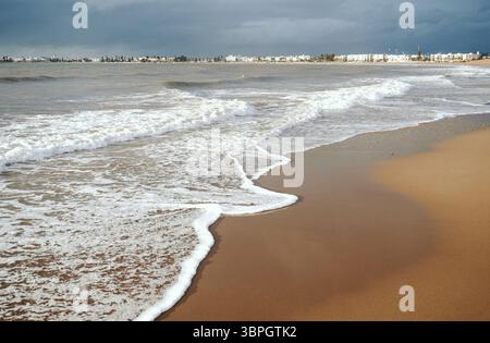 Ampia spiaggia sabbiosa con onde schiumose sotto un cielo nuvoloso a Essaouira, Marocco Foto Stock