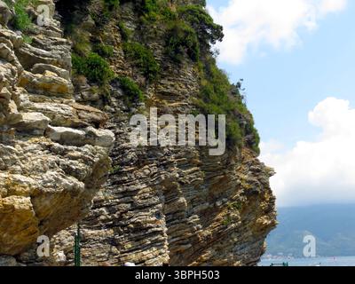 Le maestose scogliere rocciose si innalzano drammaticamente dalla costa del Montenegro, circondate da una vegetazione lussureggiante e da cieli azzurri. I visitatori apprezzano la natura Foto Stock