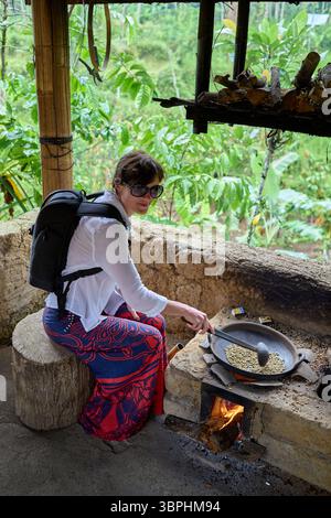 Donna che mescola i chicchi di caffè verde in una tradizionale teglia da torrefazione Foto Stock