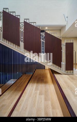 Dettaglio architettonico di una moderna scala in legno con ringhiere in pannelli di metallo e legno scuro unici. Elemento di design interno dinamico e geometrico. Foto Stock