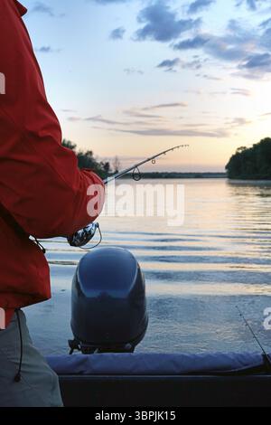 Uomo maturo che pesca dalla barca sul laghetto al tramonto Foto Stock