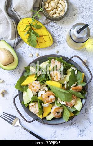 Insalata di dieta sana con rucola, spinaci, mango, avocado, gamberetti, bendaggio di pecan e vinaigrette su un tavolo in pietra grigia. Sfondo piatto con vista dall'alto Foto Stock