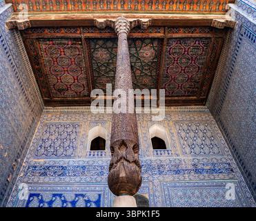Una splendida vista di un soffitto dal design intricato e di una colonna scolpita in un edificio storico, che mostra motivi ornati e colori vivaci. Foto Stock