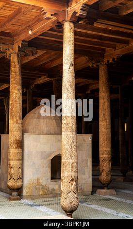 Intricate colonne scolpite in un edificio storico, che mostrano motivi e texture dettagliate. Sullo sfondo è visibile una struttura a cupola circondata Foto Stock