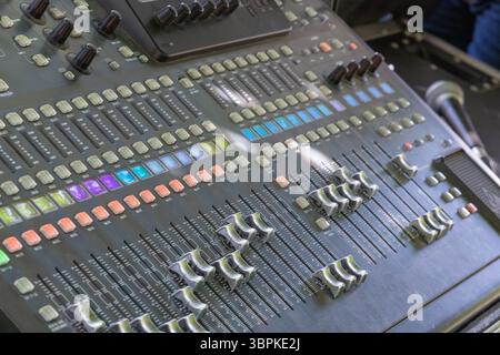 Primo piano di una sofisticata console di missaggio audio, che mette in evidenza i fader, le manopole e i pulsanti utilizzati per regolare con precisione il suono e mixare i suoni nelle professioni Foto Stock