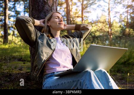 donna freelance in pausa dal lavoro, rilassati nel parco e goditi la natura mentre lavori a distanza. stile di vita digitale nomade Foto Stock