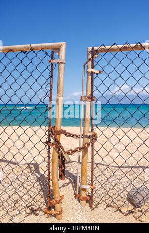 L'ingresso alla spiaggia è chiuso con una recinzione metallica e si chiude in primo piano, sabbia e mare visibili oltre Foto Stock