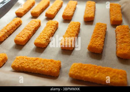 Dita di pesce in pangrattato dorato poste su carta e un vassoio da forno Foto Stock