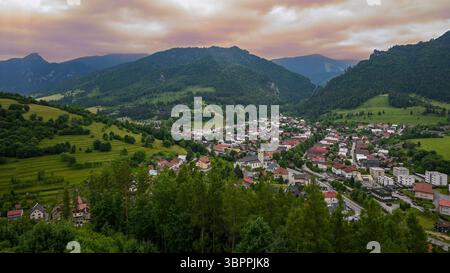 Vista mozzafiato di una piccola città annidata tra colline e montagne verdi ondulate, bagnata dal caldo bagliore del sole che tramonta. Foto Stock