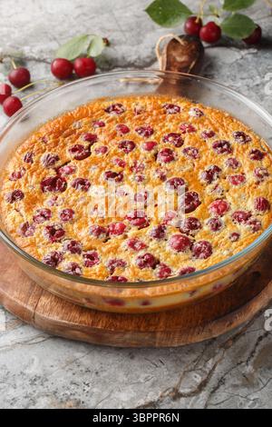 Torta estiva di clafoutis alla ciliegia con primo piano di frutti di bosco freschi in piatto da forno sul tavolo. Verticale Foto Stock