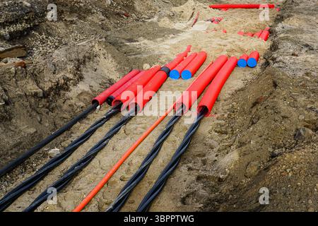 Installazione di cavi di alimentazione sotterranei con conduttori rossi protettivi presso il cantiere edile urbano Foto Stock