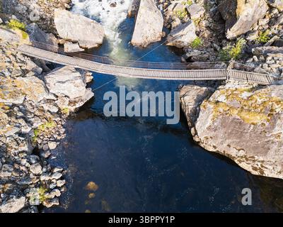 Vista aerea: Uno stretto ponte sospeso in legno che attraversa un turbolento fiume di montagna in una gola rocciosa. Natura selvaggia e turismo. Foto Stock