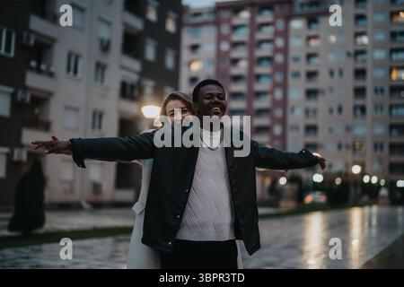 Allegra coppia multietnica che condivide un momento di gioia in un ambiente urbano durante la sera Foto Stock
