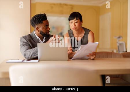 Donna d'affari seria che analizza il rapporto sulle prestazioni con un consulente finanziario maschile alla scrivania in un ufficio professionale Foto Stock