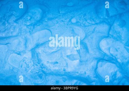Foto ravvicinata della superficie innevata di colore blu con impronte. Foto Stock