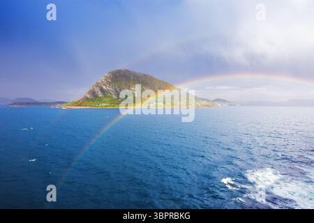 Luminosi archi arcobaleno sopra una lussureggiante isola di montagna in un fiordo norvegese, visti da una nave da crociera dopo la pioggia. Foto Stock