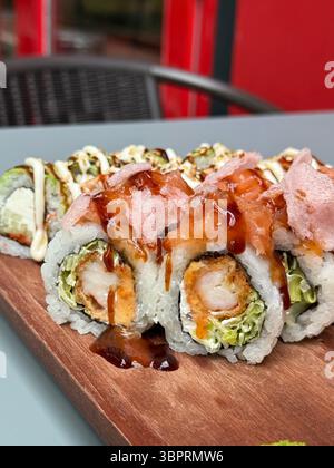 Questa immagine ravvicinata mostra i rotoli di sushi dettagliati posizionati su un vassoio di legno I panini sono ripieni di gamberi fritti, lattuga e altri ingredienti Foto Stock
