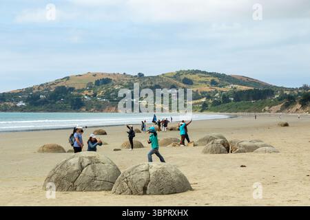 I turisti che posano con i Moeraki Boulders a Koehoe Beach, Otago Coast, South Island nuova Zelanda Foto Stock