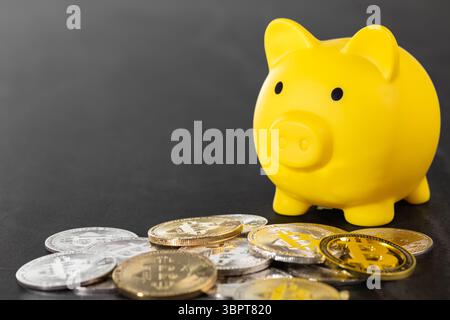 Un salvadanaio giallo circondato da monete Bitcoin in argento e oro su una superficie grigia testurizzata. L'immagine simboleggia la valuta digitale, i risparmi finanziari, Foto Stock