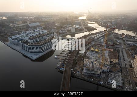 Vista aerea con drone di un paesaggio urbano al tramonto o all'alba. L'immagine mostra un grande e moderno complesso residenziale sulla riva del fiume, accanto a un vincolo principale Foto Stock