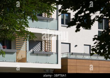 Esterno di un moderno edificio di appartamenti in una giornata di sole. La facciata presenta balconi contemporanei con ringhiere in vetro smerigliato e decorazioni in legno Foto Stock