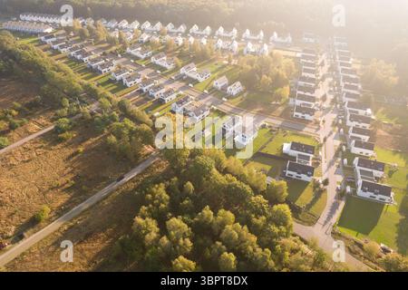 Vista aerea di un moderno complesso residenziale con case bianche identiche situate accanto a una foresta verde. Il quartiere residenziale è immerso nella Foto Stock