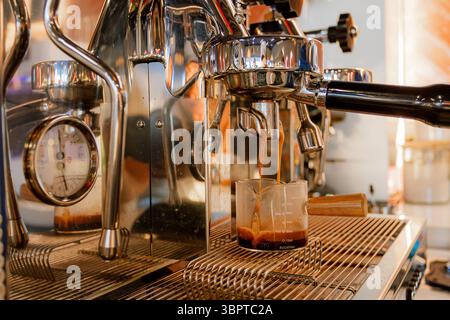 Primo piano dell'espresso appena estratto versato in un bicchiere graduato da una macchina da caffè professionale. Foto Stock