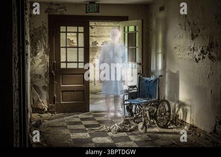 Fantasma vestito in abito da ospedale in piedi sulla porta accanto alla sedia a rotelle in abbandonato ospedale mentale, Indiana USA Foto Stock