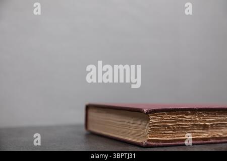 Libro antico chiuso con copertina rossa posizionata in basso a destra della cornice, messa a fuoco sui bordi della pagina tagliati in modo approssimativo, il resto della cornice lascia spazio vuoto per il testo. Foto Stock