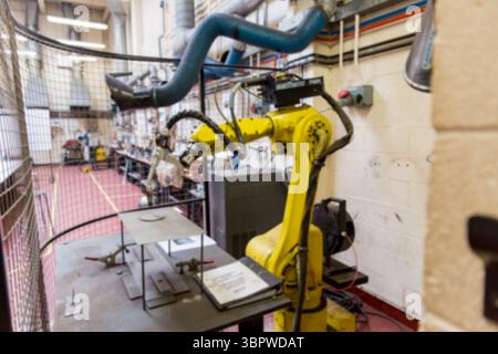 Il braccio robotico industriale giallo blocca la piastra metallica all'interno della gabbia di sicurezza in un laboratorio di progettazione piatto Foto Stock