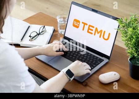 Poznan, Polonia - 15 giugno 2025: Le mani di una persona scrivono attivamente su un moderno laptop, mostrando il logo del marchio TEMU sullo schermo di un ufficio domestico Foto Stock