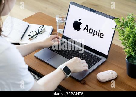 Poznan, Polonia - 15 giugno 2025: Vista ravvicinata della digitazione delle mani su un moderno laptop Apple, che mostra il logo del marchio di spicco, che riflette la modernità Foto Stock