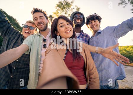 Il punto di vista in prima persona di una giovane donna che fa un divertente selfie con il suo gruppo di amici diversi e felici all'aperto, con le braccia tese in una W Foto Stock